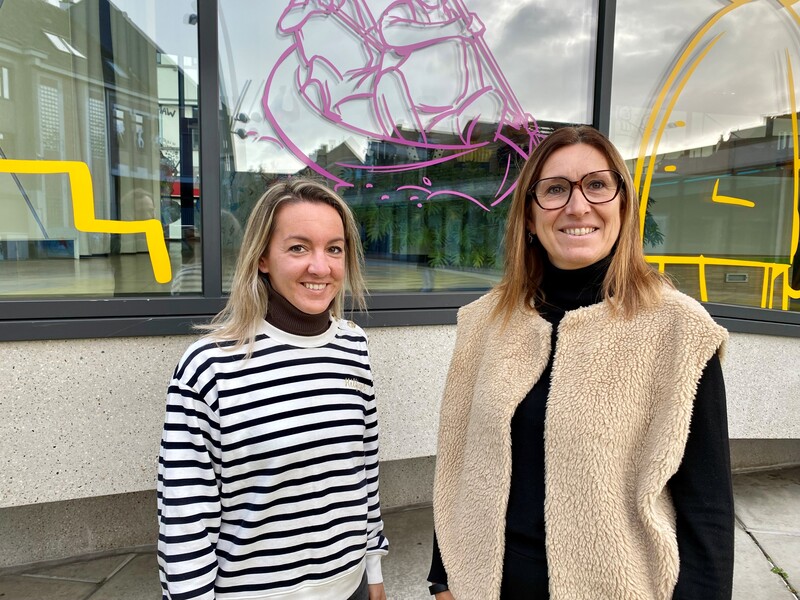 Lien en Nieke van OCMW Aalst poseren voor enkele ramen die beschilderd zijn met tekeningen.