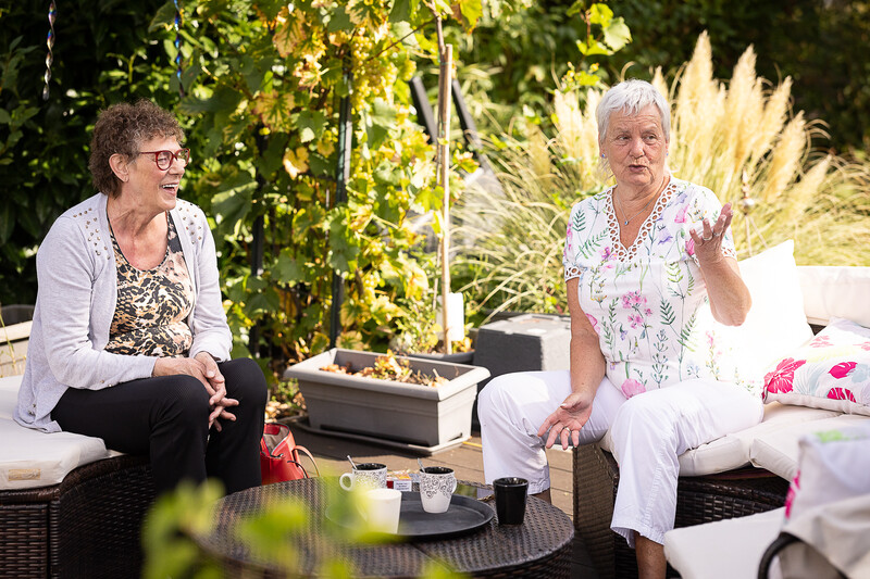 In de tuin praten 2 vriendinnen bij kop koffie.