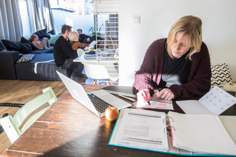 Vrouw studeert aan eettafel met kinderen en man in achtergrond