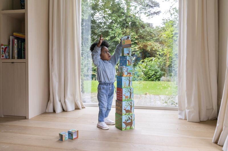 Een kind bouwt een toren met blokken in een woonkamer.