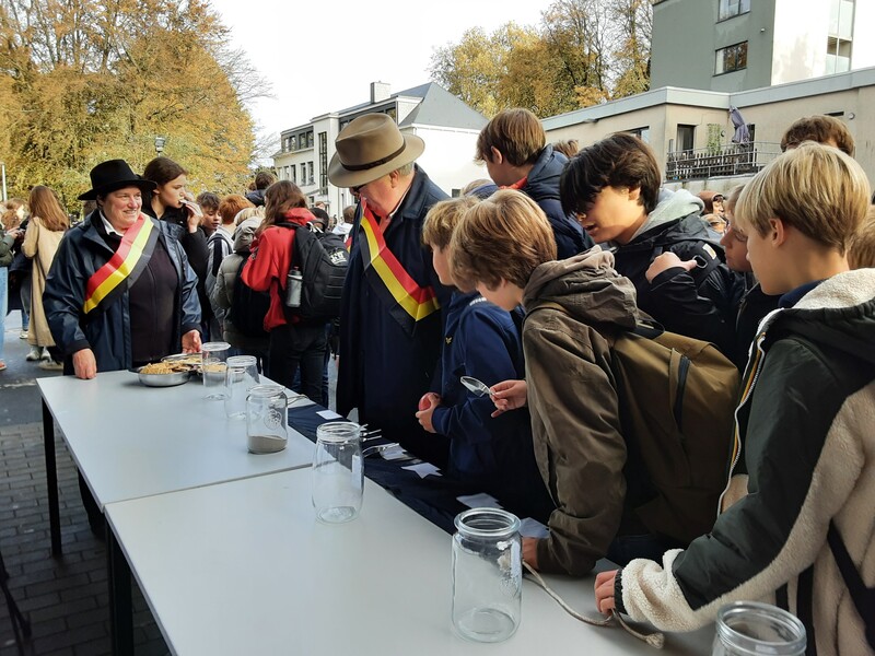 Scholieren staan aan een tafel met bokalen zand.