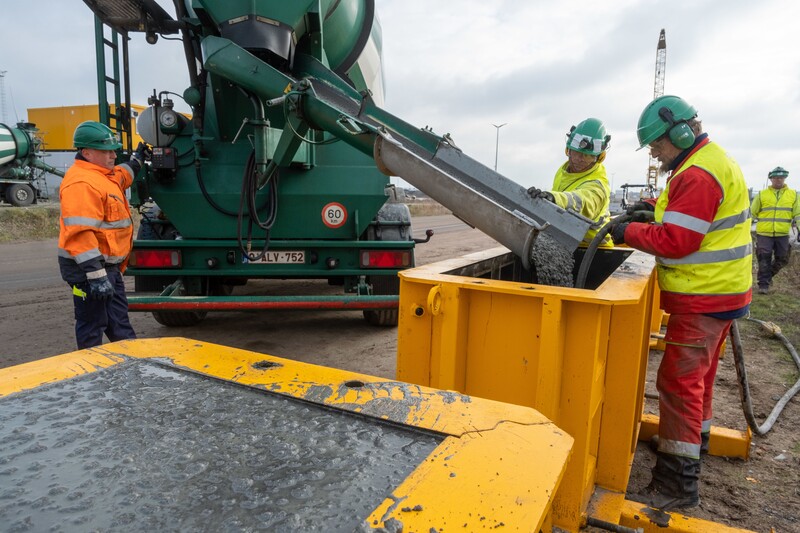 werkmannen met fluohesjes aan het werken met beton en betonwagen op achtergrond