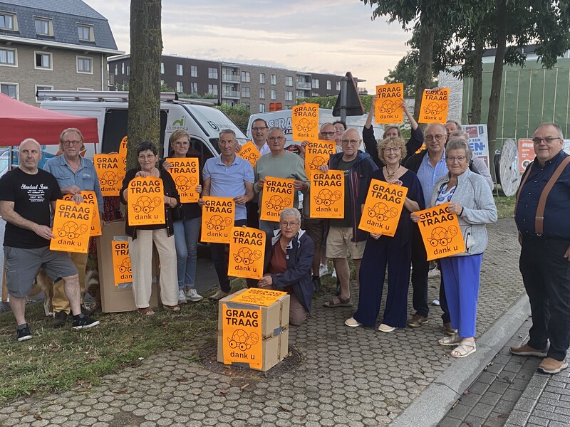 Een groep mensen staan gegroepeerd met een GRAAG TRAAG-affiche in de hand.