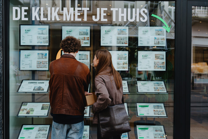 Jonge mensen voor het raam van een immokantoor met panden die te koop zijn