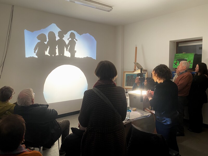 Via de beeld op een overheadprojector wordt er een verhaal verteld aan een diverse groep aandachtige luisteraars