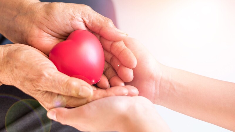 Twee paar handen houden een rood plastieken hartje vast.