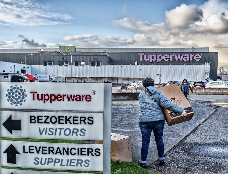 Naast de wegwijzers op de parking van de Tupperware-fabriek zeult een vrouw met een grote kartonnen doos.