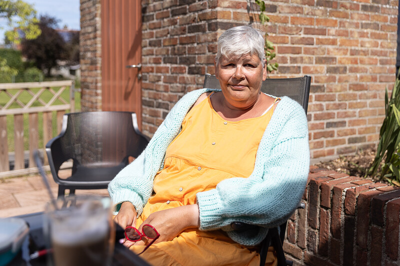 Annick Daeninck zit met een rode zonnebril in de hand op een terras en kijkt direct in de lens van de camera.