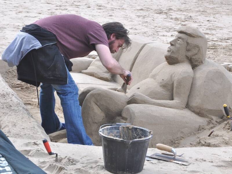 Man aan het werk aan zandsculptuur van Donald Trump
