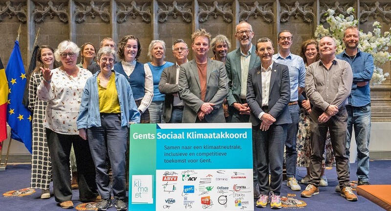Een groep van 16 personen poseert in het Gentse stadhuis bij de pancarte 'Gents Sociaal Klimaatakkoord', dat door verschillende organisaties werd ondertekend.