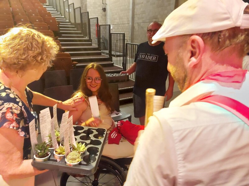 Twee vrijwilligers van bewegingspunt Oudenaarde delen een vetplantje uit aan een speelster van de Kleine Ka die in een rolstoel zit.