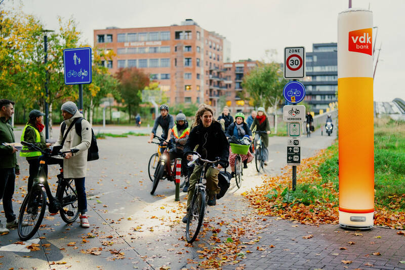 Twee medewerkers van beweging.net staan aan een fietspad en delen aan voorbijrijdende fietsers omslagen uit.