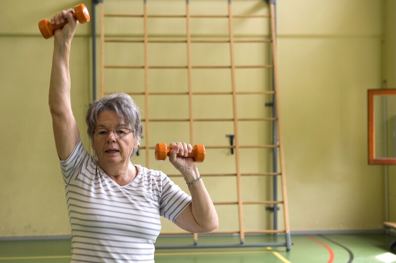 Oudere vrouw aan het sporten in turnhal met gewichten