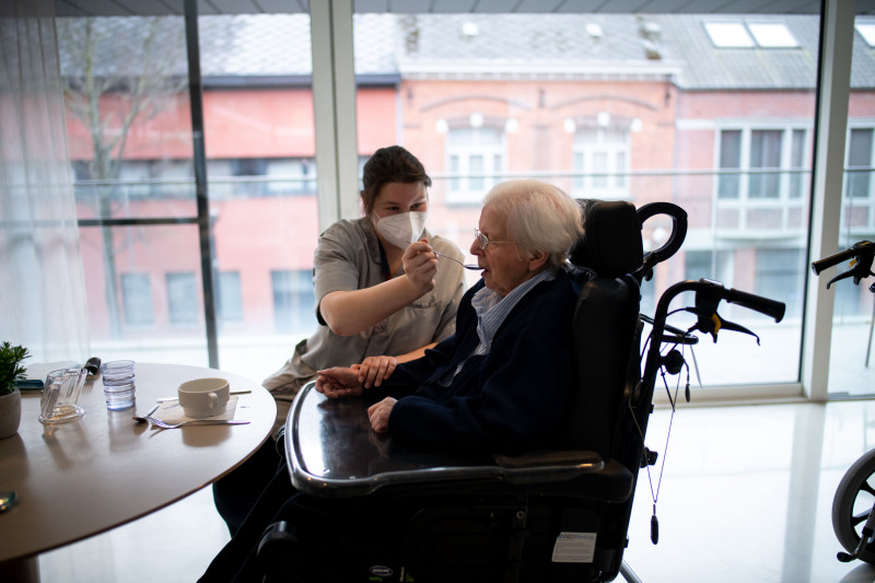 Verpleegster helpt oudere vrouw in rolstoel eten