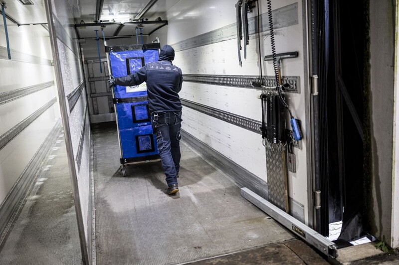 Man in werkkledij duwt kar met goederen door een magazijn.