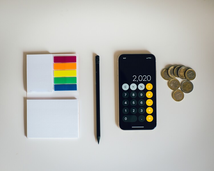 een bovenbeeld van geordende post-its, een pen, een rekenapp op een telefoon en wat kleingeld 