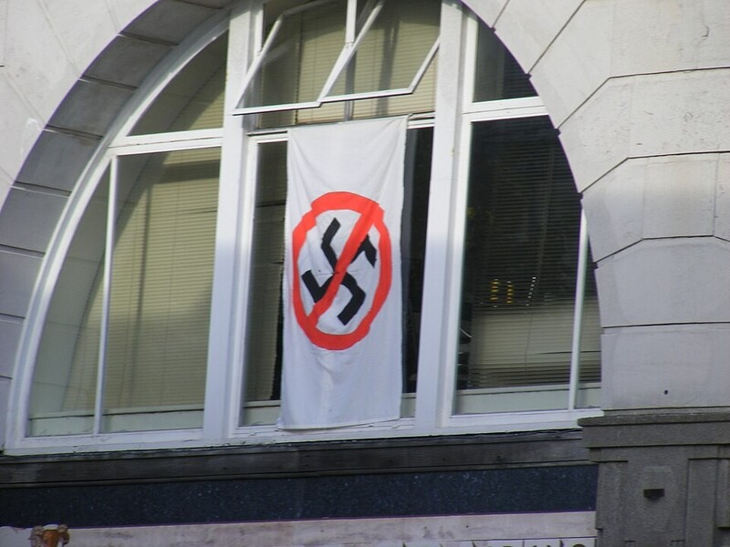Witte vlag met doorgestreept hakenkruis hangt uit raam