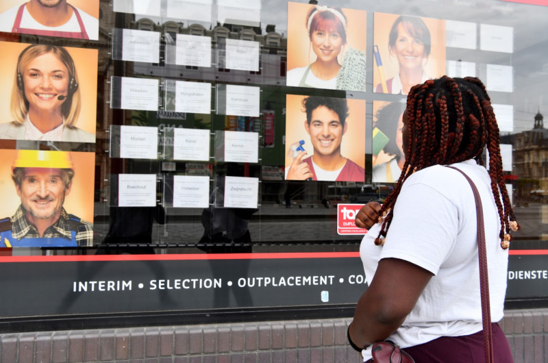 Vrouw kijkt naar vacatures in vitrine van interimkantoor.