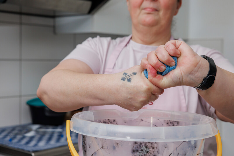 Poetshulp wringt een natte doek uit boven een emmer