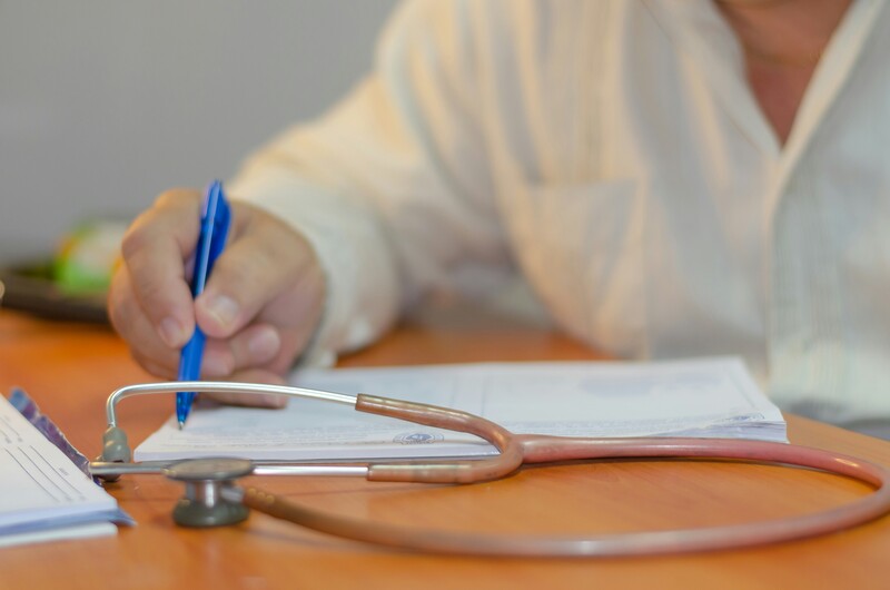 Dokter aan bureau met stethoscoop schrijft iets in document