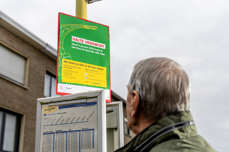 Oude man aan bushalte waarop bord hangt met aankondiging dat halte zal verdwijnen