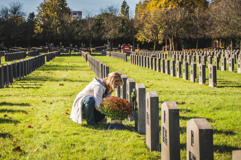 Vrouw kuist graf en plaatst chrysanten op Allerheiligen