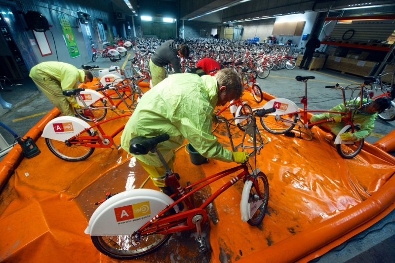Jobstudenten kuisen vuile stadsfietsen van Antwerpen op oranje plastiekfolie in magazijn