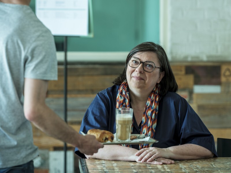 Journaliste en auteur Nathalie Le Blanc in een koffiebar terwijl een ober een koffie serveert