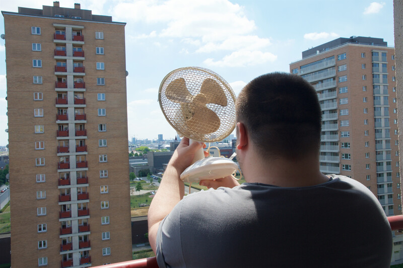 Man met ventilator op balkon van flatgebouw