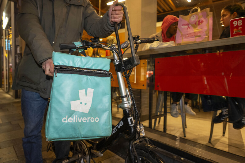 Een platformwerker van Deliveroo staat buiten voor een snackbar