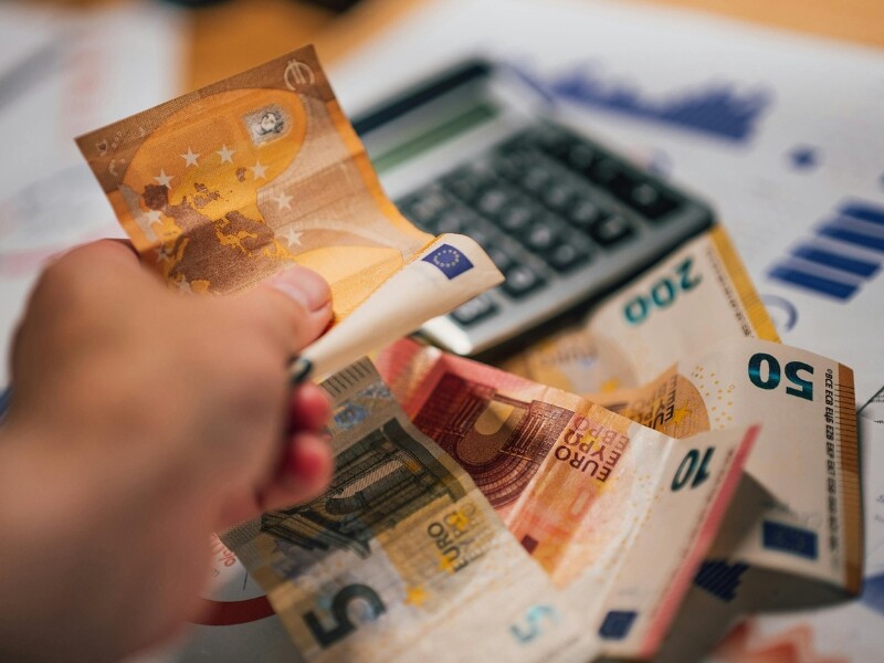 hand met 10 euro biljet en eurobiljetten op tafel