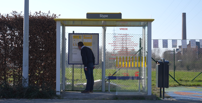 Dieter staat aan bushokje en kijkt naar uurtabel.