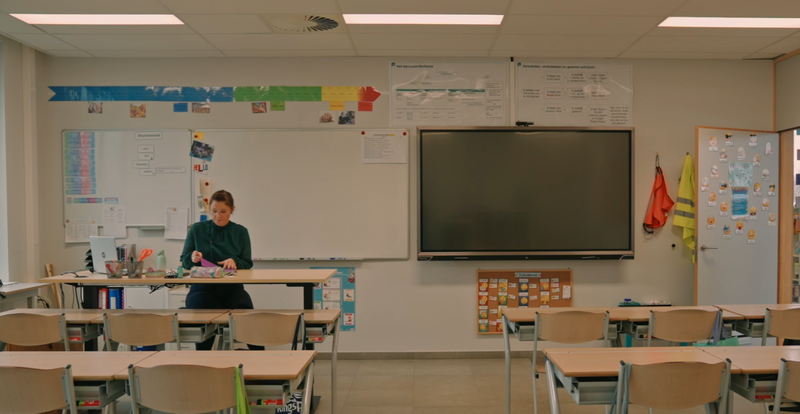 Een leerkracht zit aan haar bureau in een leeg klaslokaal