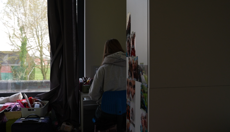 Zestienjarige scholier zit aan bureau in haar kamer.