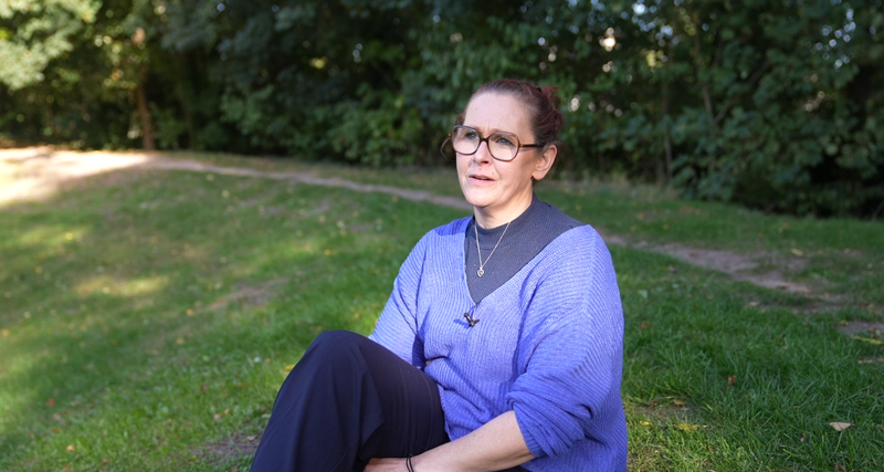 Vrouw met blauwe trui en bril zit op het grasveld.