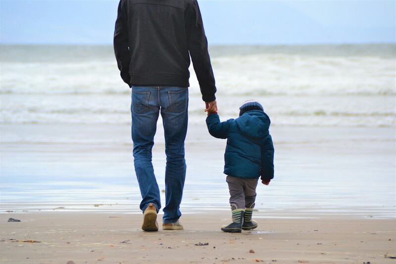 Man hand in hand met peuter aan het wandelen op strand