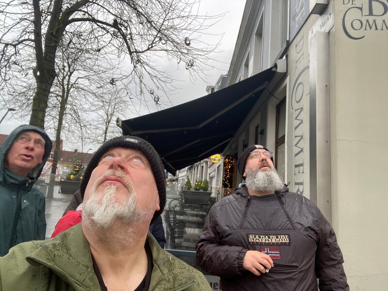 Drie mannen kijken omhoog op zoek naar camera's in het straatbeeld.