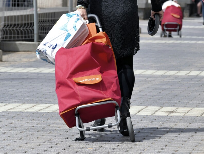 close-up van de benen van een oudere vrouw met een kapot shoppingkarretje